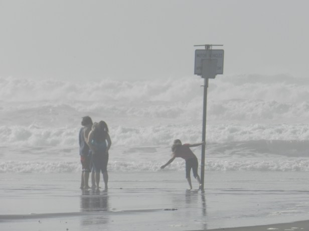 Kids swinging off of a warning sign in the pending surf.